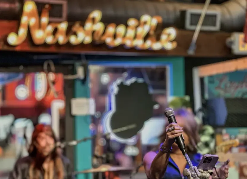 Two singers at a bar in with a lit up Nashville sign
